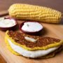 A closeup of cachapa with cheese and boiled corn on the background